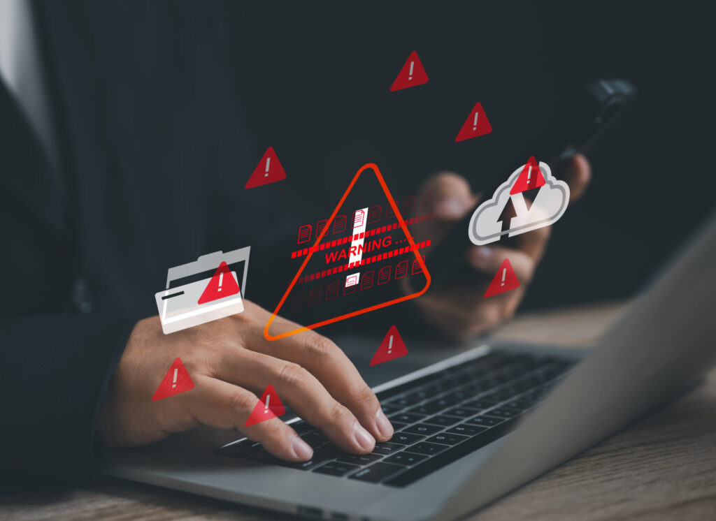 businessman works on a laptop surrounded by red warning icons, symbolizing cybersecurity threats, data security issues, and the urgent need for protection against digital vulnerabilities and breaches.